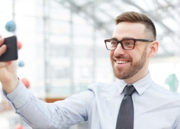 Imagem de um home em traje corporativo fazendo usando a câmera frontal de seu celular