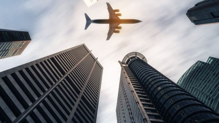 Avião passando por vários prédios em um céu com nuvens
