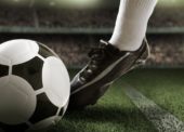 Imagem de uma pessoa usando chuteiras e chutando uma bola de futebol