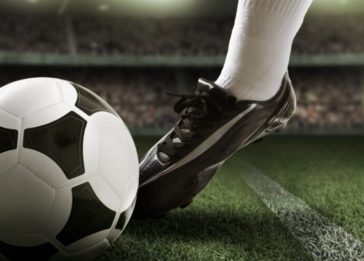 Imagem de uma pessoa usando chuteiras e chutando uma bola de futebol