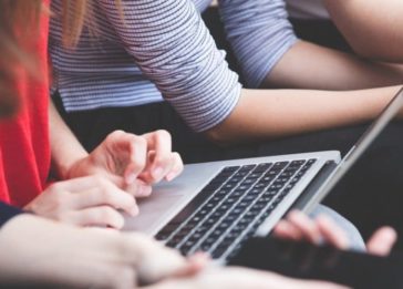 Imagem de diversas pessoas participando de uma reunião. Uma delas está mexendo em um laptop, enquanto outros mexem no celular
