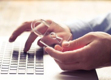Mãos de um homem segurando um cadeado enquanto digita no teclado de um notebook