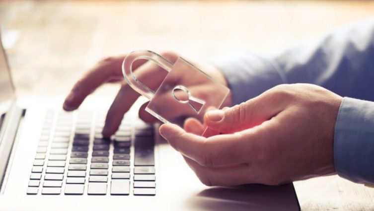 Mãos de um homem segurando um cadeado enquanto digita no teclado de um notebook
