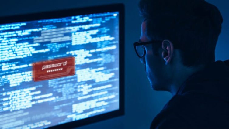 Imagem de um homem olhando para a tela de um computador. Há um aviso na tela com a palavra "senha" escrito.