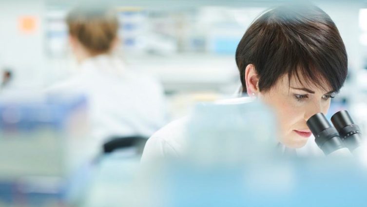 Mulher cientista analisa algo no microscópio