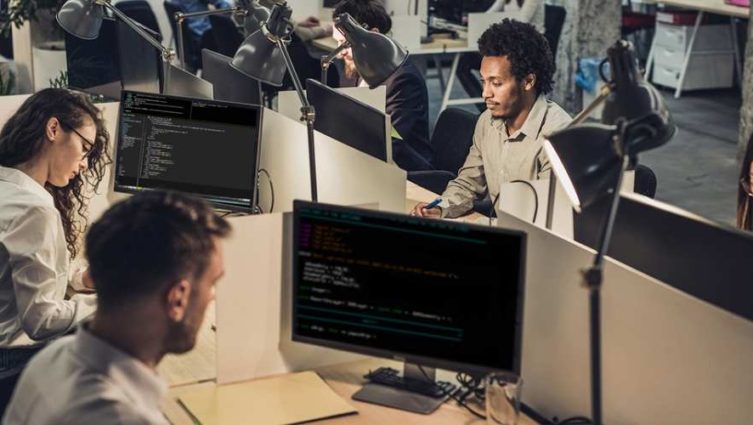 Homens e mulheres trabalhando na frente de vários computadores, usados para blockchain