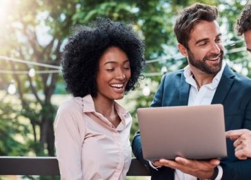 Três executivos - uma mulher negra e dois homens brancos - acessam a internet em um notebook