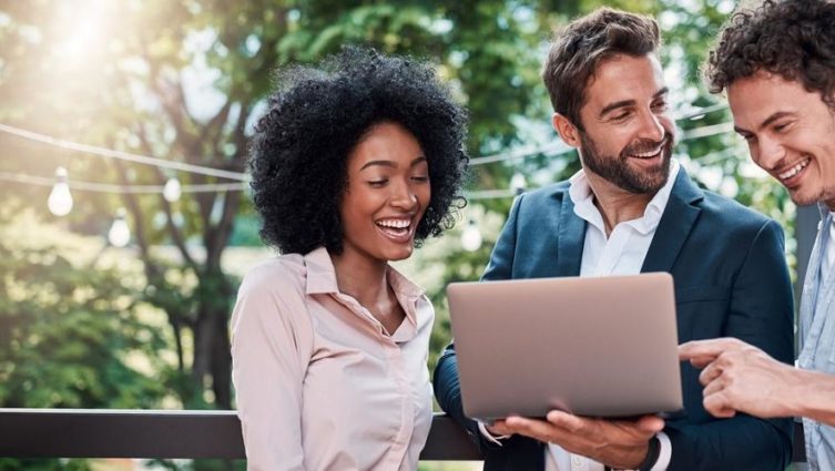 Três executivos - uma mulher negra e dois homens brancos - acessam a internet em um notebook