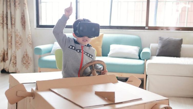Criança com óculos de realidade virtual brinca em carro feito de papelão - futuro