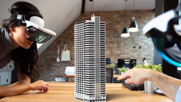 Jovem com óculos de realidade virtual observa a maquete de um edifício