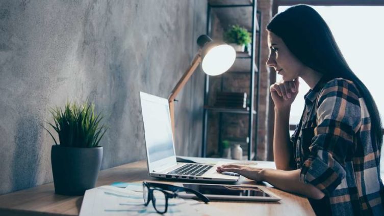 Mulher sentada em um escritório olha para a tela de seu computador enquanto trabalha