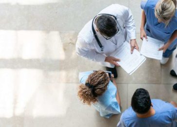 Imagem de uma reunião em círculo de 5 profissionais de saúde em um hospital
