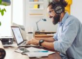Homem realiza trabalho em casa, a partir de seu laptop, enquanto utiliza um fone de ouvido