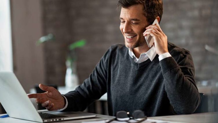 Imagem de um executivo conversando no celular enquanto trabalha no laptop